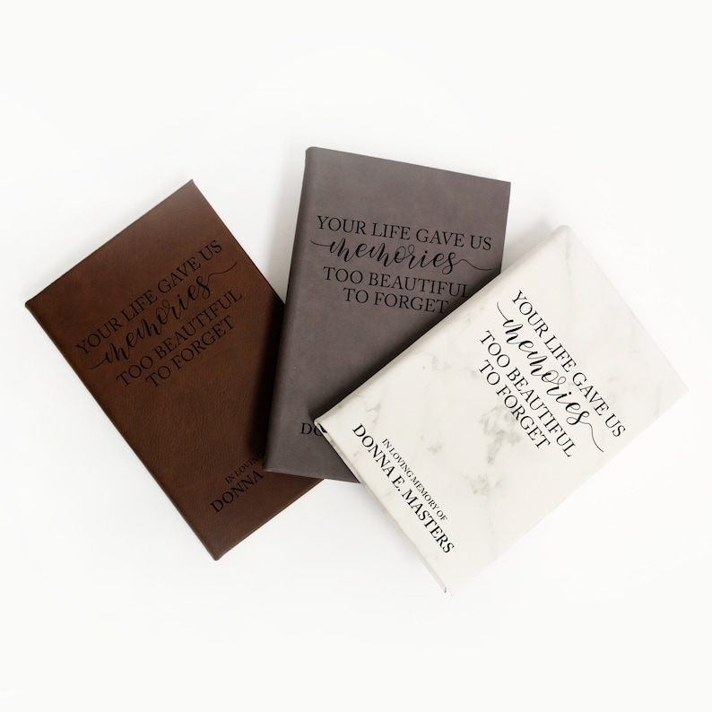 May include: Three memorial journals in brown, gray, and white marble patterns. Each journal has the inscription "YOUR LIFE GAVE US memories TOO BEAUTIFUL TO FORGET" and the name "DONNA E. MASTERS".