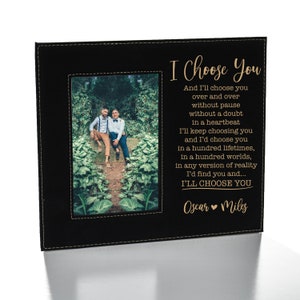 May include: A black leather photo frame with a gold inscription that reads "I Choose You" and "Oscar Miles". The frame has a photo of two people standing in a garden.