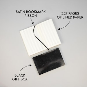 May include: A black gift box containing a white notebook. The notebook has 227 lined pages and a black satin ribbon bookmark.