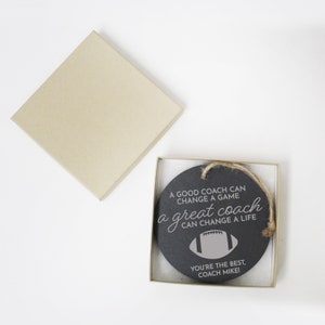 May include: A black round chalkboard ornament with a white inscription that reads "A good coach can change a game, a great coach can change a life."  The ornament also features a gray football graphic and the text "You're the best, Coach Mike!"