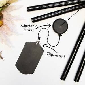 May include: Black wind chime with an adjustable striker and a clip-on sail. The striker is attached to a black cord and the sail is a black rectangle.