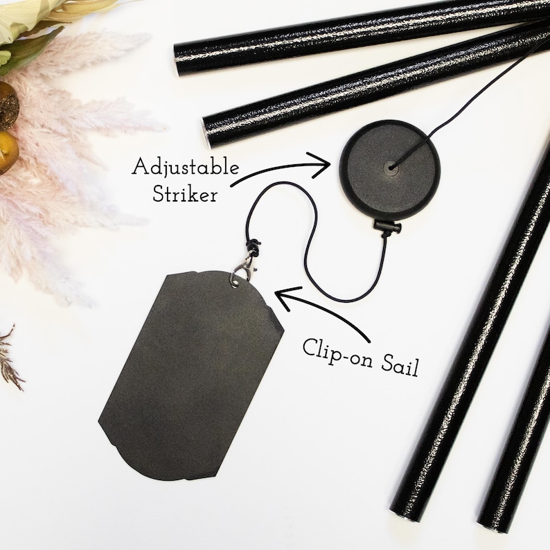 May include: Black wind chime with an adjustable striker and a clip-on sail. The striker is attached to a black cord and the sail is a black rectangle.