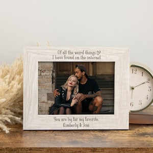 May include: A white wooden picture frame with the text "Of all the weird things I have found on the internet" and "You are by far my favourite. Kimberly & José". The frame holds a photo of a couple. A gold clock is to the right.