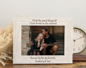 Può includere: Una cornice in legno bianco con il testo "Of all the weird things I have found on the internet" e "You are by far my favorite. Kimberly & José". La cornice contiene una foto di una coppia. Un orologio dorato è a destra.
