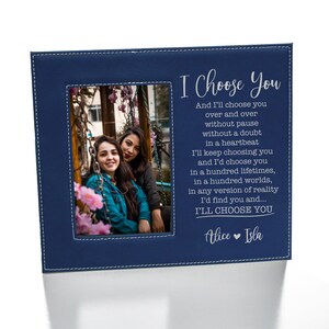 May include: A blue leatherette photo frame with a stitched border. The frame has a photo of two women smiling at the camera. The text "I Choose You" is printed in white on the frame, along with a poem about choosing someone over and over again. The names "Alice" and "Isla" are printed at the bottom of the frame.