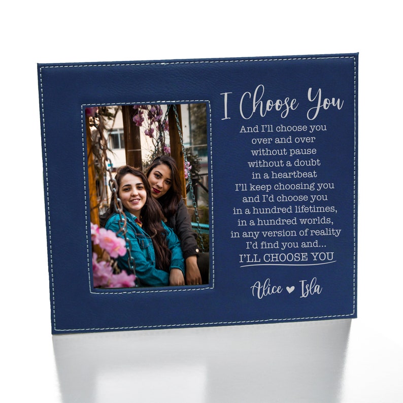 May include: A blue leatherette photo frame with a stitched border. The frame has a photo of two women smiling at the camera. The text "I Choose You" is printed in white on the frame, along with a poem about choosing someone over and over again. The names "Alice" and "Isla" are printed at the bottom of the frame.
