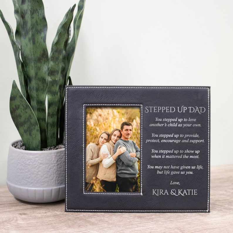 Peut inclure: Un cadre photo en cuir noir avec des coutures blanches et une inscription argent&eacute;e qui dit "Stepped Up Dad". L'inscription comprend un message sinc&egrave;re sur l'amour et le soutien d'un beau-parent. Le cadre comprend une photo de famille.