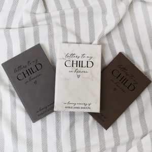 May include: Three gray, brown, and white journals with the text "letters to my child in heaven" on the front. The white journal has a marble pattern and the text "in loving memory of AVERIE JAMES BARTON".