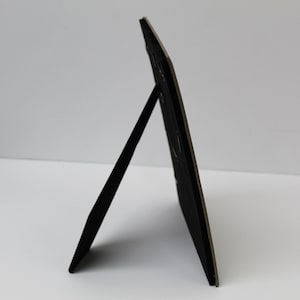 May include: A black picture frame with a stand on the back. The frame is made of a sturdy material and has a simple design.