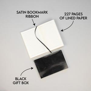 May include: A black gift box with a white notebook inside. The notebook has 227 lined pages and a black satin ribbon bookmark.