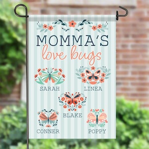 May include: A personalized garden flag with the text "Momma's love bugs" in navy and coral. The flag features butterfly illustrations with names: Sarah, Linea, Blake, Conner, and Poppy. The background has vertical stripes.