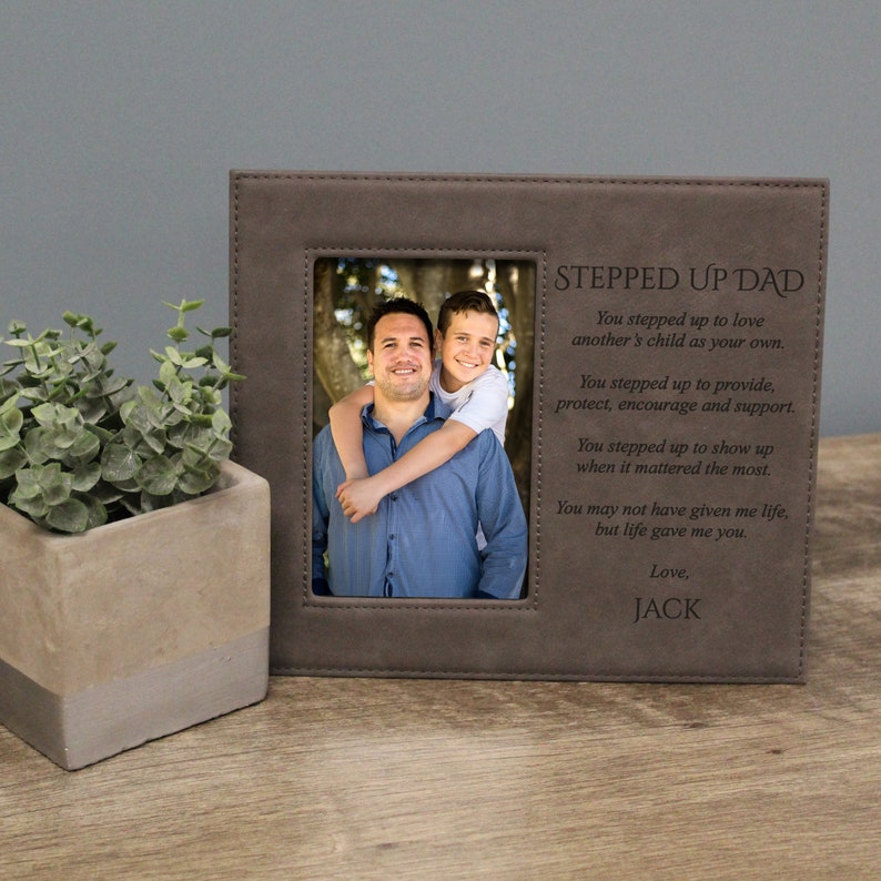 A brown leatherette picture frame with a photo of two people. The frame has the words 'Stepped Up Dad' and a poem about a stepfather engraved on it. The poem reads: 'You stepped up to love another's child as your own. You stepped up to provide, protect, encourage and support. You stepped up to show up when it mattered the most. You may not have given me life, but life gave me you. Love, Jack.'