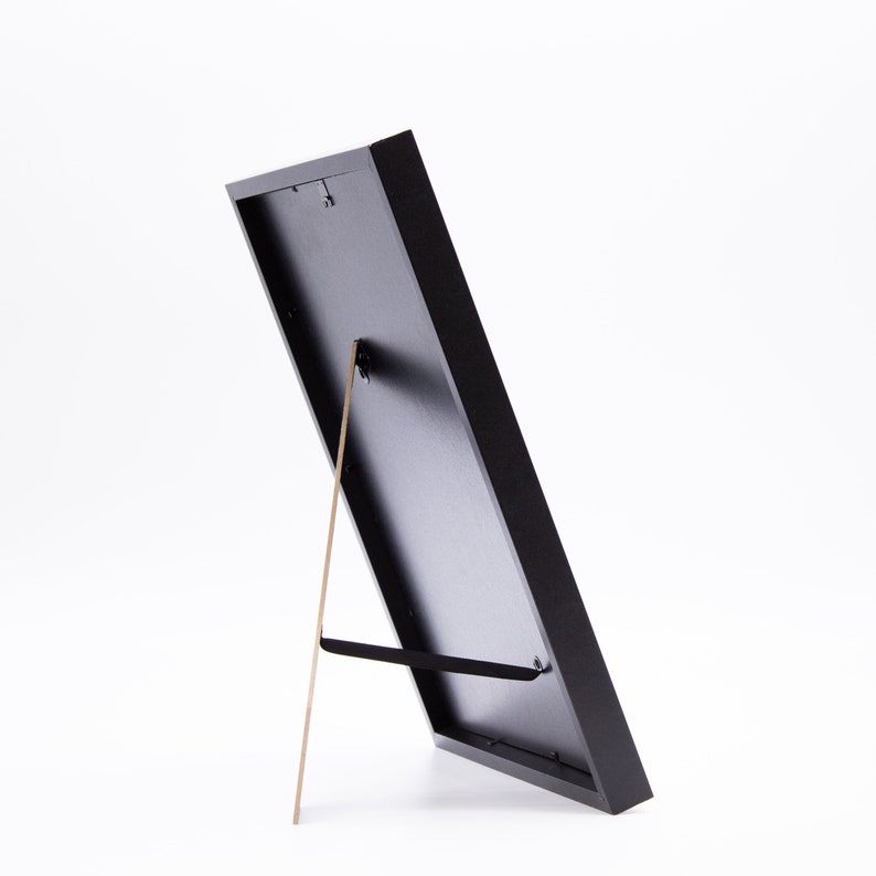 May include: A black picture frame with a built-in easel stand. The frame is made of wood and has a matte finish.