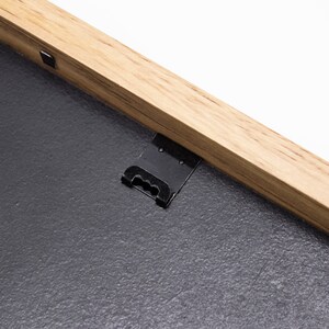 May include: A close-up of a black metal hanging hook attached to the back of a wooden picture frame.