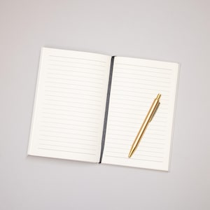 May include: An open notebook with lined pages and a gold pen lying on the right page.