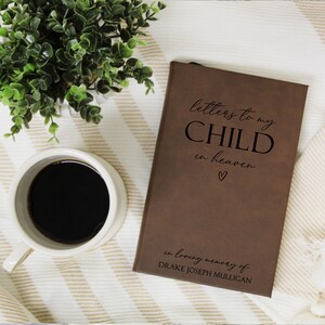 May include: A brown leather journal with the text "letters to my CHILD in heaven" and a small heart symbol. The journal is inscribed with "in loving memory of DRAKE JOSEPH MULLIGAN".