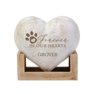 May include: White heart-shaped stone with a paw print and the text "Forever in our hearts GROVER" engraved on it. The stone is sitting on a wooden stand.