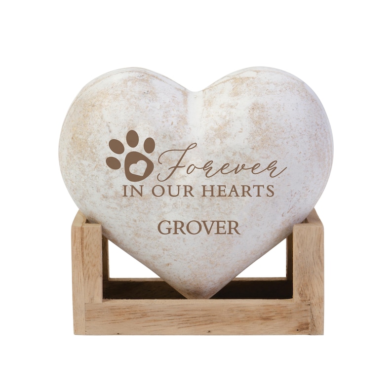 May include: White heart-shaped stone with a paw print and the text "Forever in our hearts GROVER" engraved on it. The stone is sitting on a wooden stand.