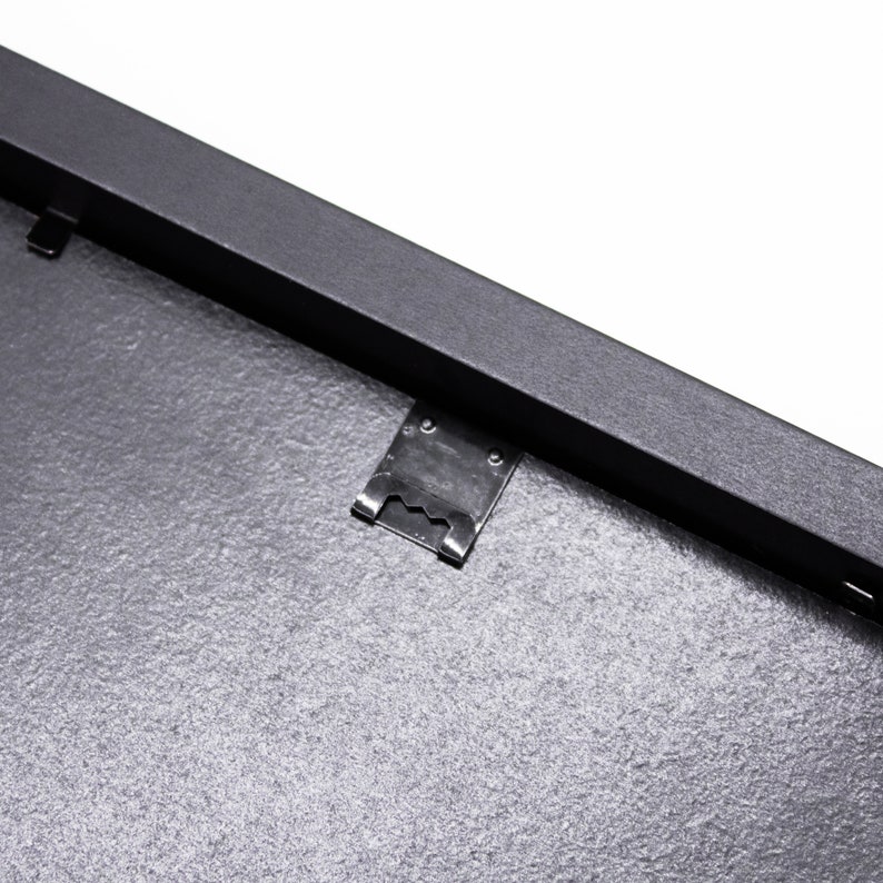 May include: Close-up of a black picture frame with a metal hanging clip. The frame has a textured surface.