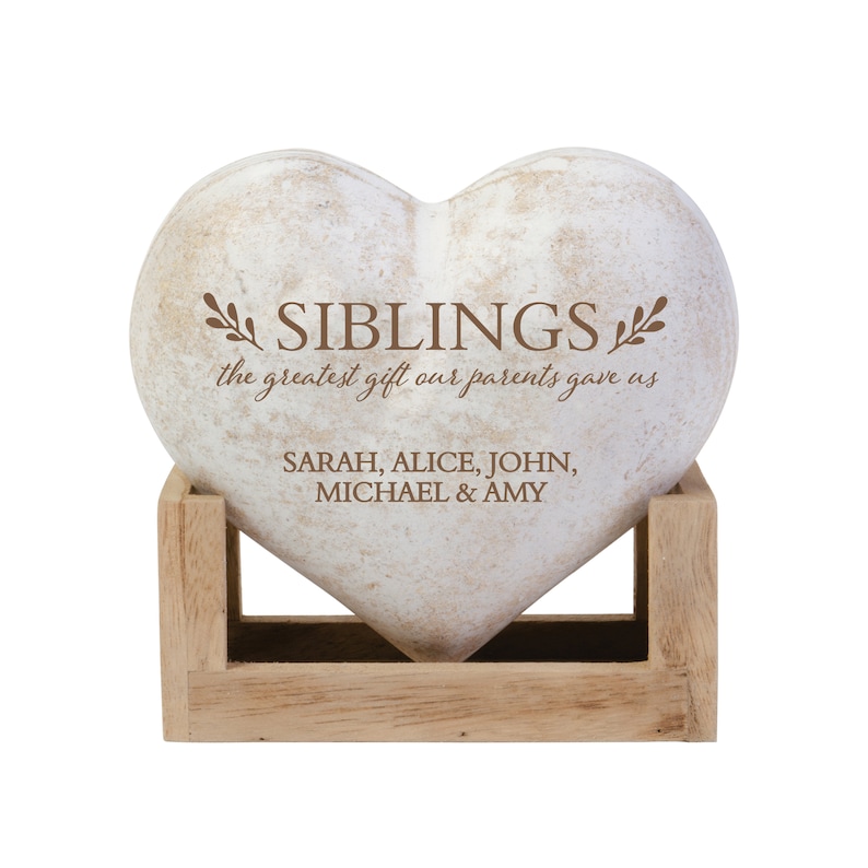 May include: White heart-shaped stone with the words "Siblings, the greatest gift our parents gave us" and the names "Sarah, Alice, John, Michael & Amy" engraved on it. The stone is sitting on a wooden stand.