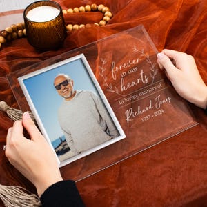 K&ouml;nnte beinhalten: Ein klarer Glasbilderrahmen mit silbernem Rand. Der Rahmen enth&auml;lt ein Foto eines Mannes. Der Rahmen ist mit dem Text "forever in our hearts" und "In loving memory of Richard Jones 1957-2024" graviert.