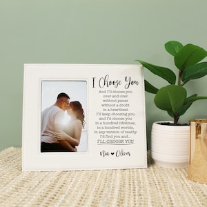 May include: White photo frame with a stitched border and a black and white photo of a couple. The frame has a quote that reads "I Choose You" and "And I'll choose you over and over without pause without a doubt in a heartbeat I'll keep choosing you and I'd choose you in a hundred lifetimes, in a hundred worlds, in any version of reality I'd find you and... I'LL CHOOSE YOU" with the names "Nia Oliver" at the bottom.