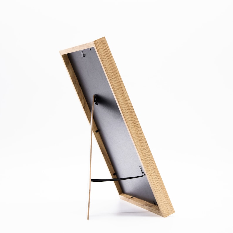 May include: A wooden picture frame with a black mat and a stand on the back. The frame is standing on a white surface.