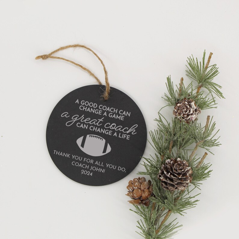 May include: A black round chalkboard ornament with a white inscription that reads "A good coach can change a game, a great coach can change a life."  The ornament also features a white football graphic and the text "Thank you for all you do, Coach John! 2024".