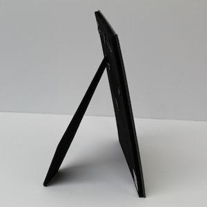 May include: Black picture frame with a stand on the back. The frame is made of cardboard and has a matte finish.