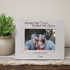 May include: A white wooden picture frame with a photo of two dads and their child. The frame has the text "Double the Dads, Double the Love" and "I love you both! Jess".
