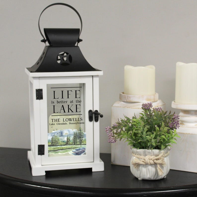 May include: White lantern with a black top and a glass window. The glass window has a watercolor painting of a lake scene and the text "Life is better at the lake. The Lowells. Lake Glendale, Pennsylvania."