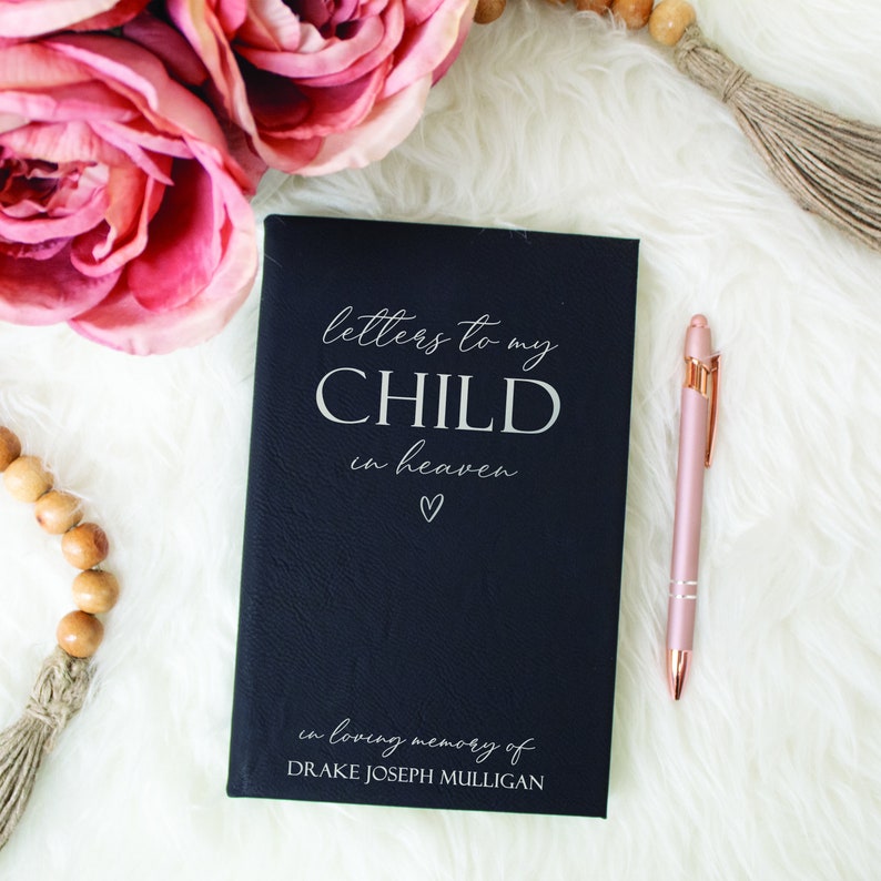 May include: A black leather-bound journal with the title "Letters to my Child in Heaven" in white lettering. The journal also includes the text "in loving memory of DRAKE JOSEPH MULLIGAN" in white lettering.
