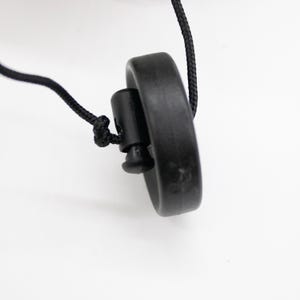 Op de afbeelding: Een zwart koord met een zwarte plastic toggle en een zwarte ronde schijf aan het einde.