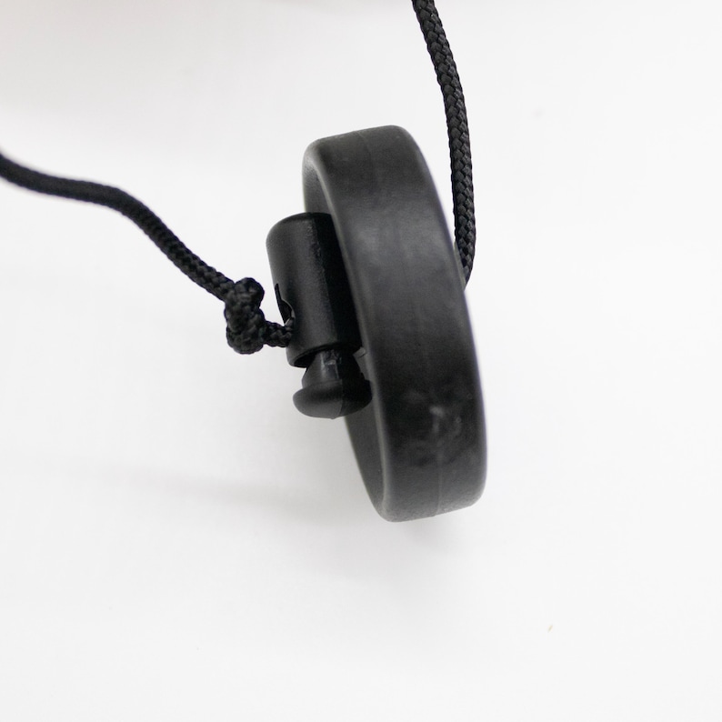 Op de afbeelding: Een zwart koord met een zwarte plastic toggle en een zwarte ronde schijf aan het einde.