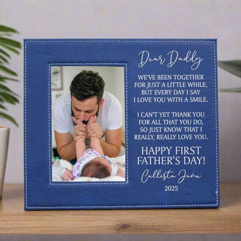 Blue First Father's Day Picture Frame with "Dear Daddy" Poem and personalized with baby's name in carmel brown sitting on an end table with a plant