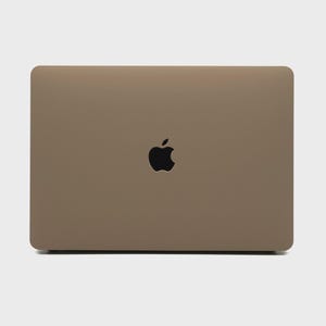 May include: A closed, tan-colored laptop with a black Apple logo centered on the lid. The laptop has rounded corners and a smooth surface, suggesting a modern design.