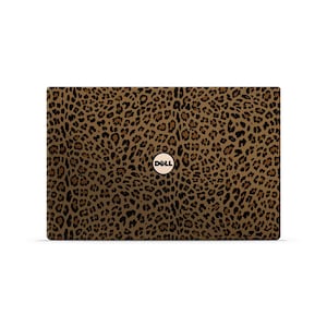Peut inclure: Un ordinateur portable avec un motif léopard. Le couvercle présente un motif tacheté marron et noir, avec le logo Dell au centre. L'ordinateur portable est rectangulaire et semble fermé.