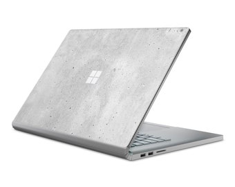 May include: A silver laptop with a concrete-patterned design on the lid. The laptop is open and the screen is facing away from the viewer. The Microsoft logo is visible on the lid.