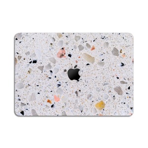 Puede incluir: Una piel de port&aacute;til blanca con un patr&oacute;n de terrazo. La piel tiene peque&ntilde;as motas negras, blancas, marrones y rosas por todas partes. El logotipo de Apple es visible en el centro de la piel.