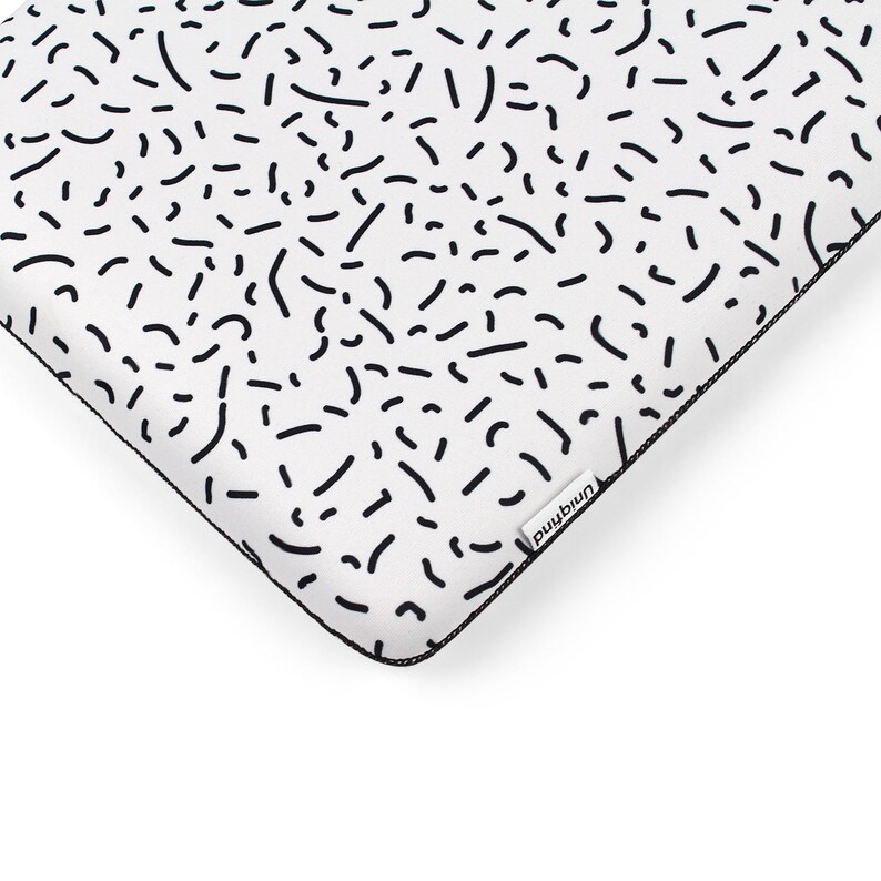 Puede incluir: Funda para port&aacute;til blanca con un patr&oacute;n geom&eacute;trico en blanco y negro. La funda tiene una cremallera negra y una peque&ntilde;a etiqueta negra con la palabra "mind" impresa en ella.