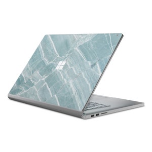 May include: A silver laptop with a light blue marble design on the lid. The laptop is closed and the lid is slightly open. The Microsoft logo is visible on the lid.