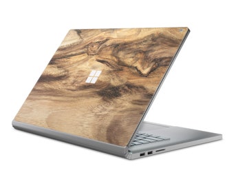 May include: A silver laptop with a wood grain design on the lid. The laptop is closed and the lid is open at a slight angle. The Microsoft logo is visible on the lid.