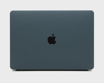 Könnte beinhalten: Ein geschlossener, dunkelblauer Laptop mit abgerundeten Ecken. Das Apple-Logo ist mittig auf dem Deckel in Schwarz angebracht. Der Laptop steht vor einem schlichten, hellen Hintergrund.