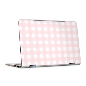 May include: A laptop featuring a pink and white gingham pattern on the lid. The laptop is silver and has a screen that is slightly open. The gingham pattern is a classic design.