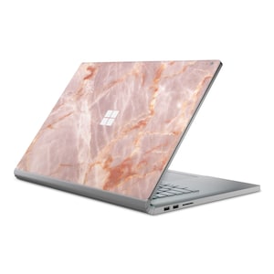 May include: A silver laptop with a pink and orange marble design on the lid. The laptop is closed and the lid is open to a 45-degree angle. The Microsoft logo is visible on the lid.