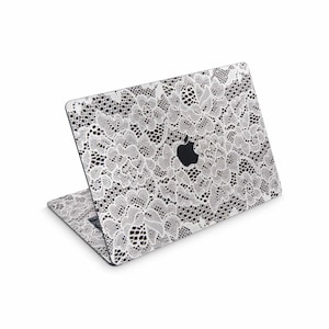 May include: A laptop with a white lace design skin. The skin covers the top and keyboard area of the laptop. The Apple logo is visible on the top of the laptop. The lace pattern is detailed and covers the entire surface.
