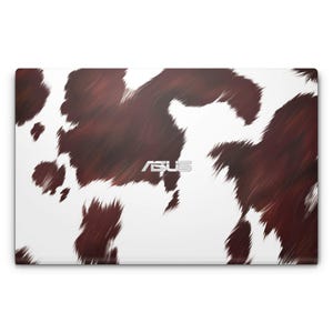 May include: White laptop with a brown and white cowhide pattern. The ASUS logo is in the centre of the laptop.