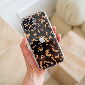 May include: A clear phone case with a tortoiseshell pattern. The case has a raised camera bump and a cutout for the Apple logo.