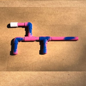 May include: A pink and blue PVC pipe toy gun. The gun has a white plastic nozzle and is made of multiple pieces of pipe connected together.