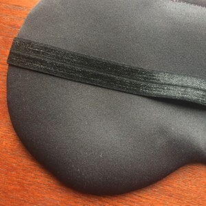 Op de afbeelding: Zwarte slaapmasker met een verstelbare elastische band. Het masker is gemaakt van een zacht, comfortabel materiaal.